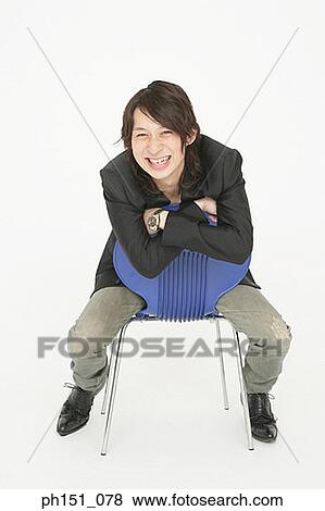 Portrait of a young man sitting on a chair and looking cheerful View Large Photo Image Stock Photo - Portrait of a young man sitting on a chair and looking cheerful. Fotosearch