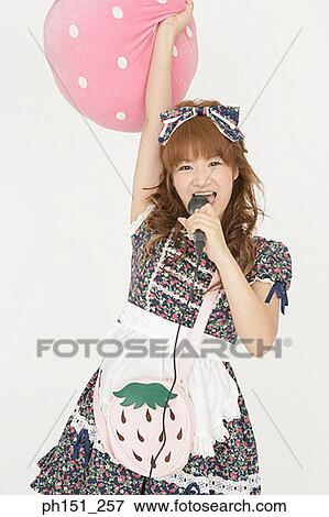 Stock Photo - Portrait of a young woman holding a cushion and singing into a microphone. Fotosearch