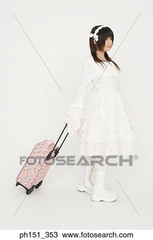 Stock Image - Side profile of a young woman pulling her luggage. Fotosearch