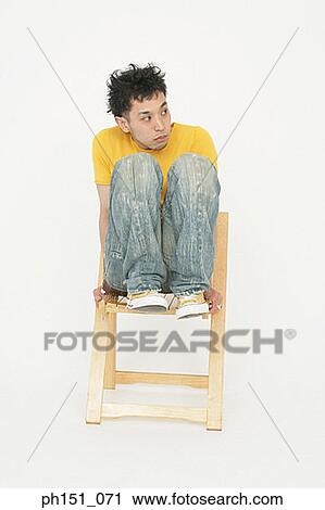 Young man balancing on a wooden chair and looking away View Large Photo Image Stock Image - Young man balancing on a wooden chair and looking away. Fotosearch