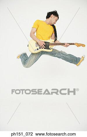 Stock Image - Young man playing an electric guitar and jumping. Fotosearch