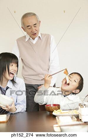 Boy and a girl sitting at the dining table with their grandfather standing behind them View Large Photo Image Picture - Boy and a girl sitting at the dining table with their grandfather standing behind them. Fotosearch