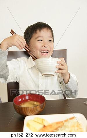 Stock Image - Close-up of a boy holding a bowl and a pair of chopsticks. Fotosearch