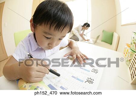 Stock Image - Close-up of a boy writing on a sheet of paper with his sister using a laptop in the background. Fotosearch
