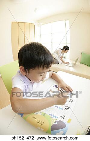 Stock Image - Close-up of a boy writing on a sheet of paper with his sister using a laptop in the background. Fotosearch