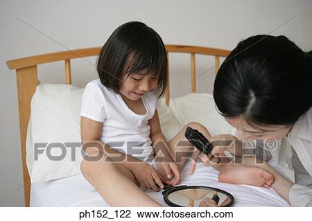 Stock Image - Close-up of a girl and her mother looking at a hand mirror on the bed. Fotosearch