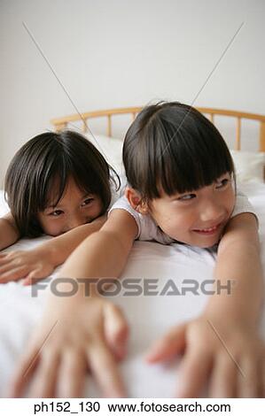 Stock Image - Close-up of a girl and her sister lying on the bed and smiling. Fotosearch