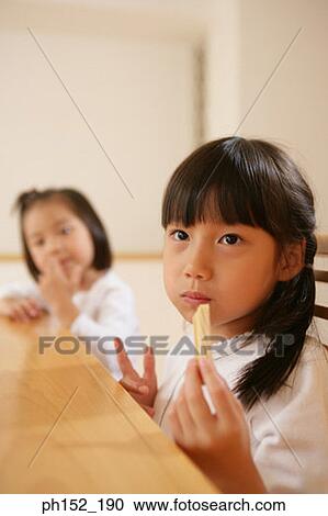 Stock Image - Close-up of a girl eating French fries with her sister sitting beside her. Fotosearch