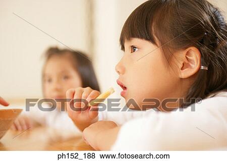 Close-up of a girl eating French fries with her sister sitting beside her View Large Photo Image Stock Photo - Close-up of a girl eating French fries with her sister sitting beside her. Fotosearch