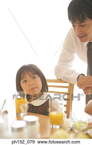 Close-up of a girl sitting at a dining table with her father standing behind her View Large Photo Image Stock Photo - Close-up of a girl sitting at a dining table with her father standing behind her. Fotosearch