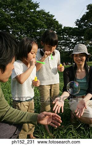 Stock Image - Close-up of a mid adult couple and their two daughters blowing bubbles in a park. Fotosearch