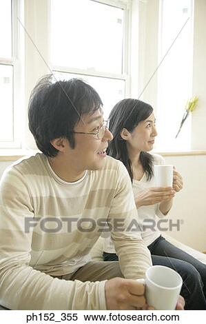 Close-up of a mid adult couple sitting on a couch and holding cups of coffee View Large Photo Image Stock Photography - Close-up of a mid adult couple sitting on a couch and holding cups of coffee. Fotosearch
