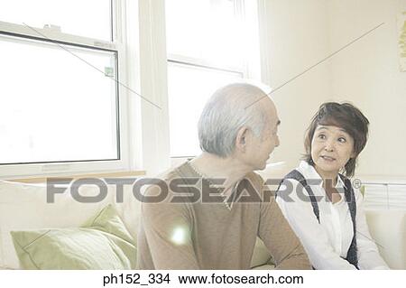 Picture - Close-up of a senior couple sitting on a couch and looking at each other. Fotosearch