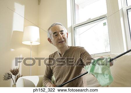 Stock Image - Close-up of a senior man sitting on a couch and cleaning a golf club. Fotosearch