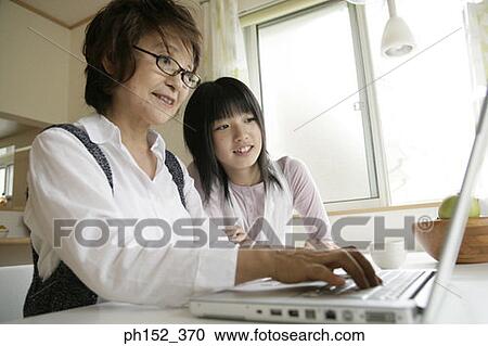 Stock Image - Close-up of a senior woman using a laptop with her granddaughter sitting beside her. Fotosearch