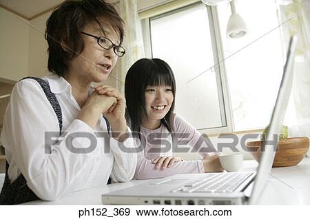 Stock Photo - Close-up of a senior woman using a laptop with her granddaughter sitting beside her. Fotosearch