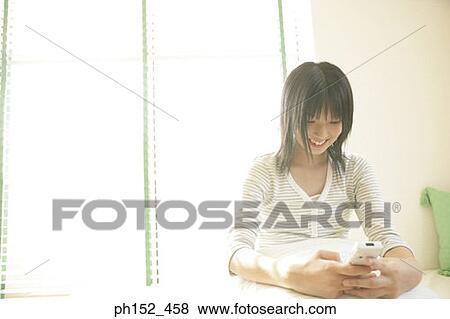 Close-up of a young woman holding a mobile phone and smiling View Large Photo Image Stock Photo - Close-up of a young woman holding a mobile phone and smiling. Fotosearch