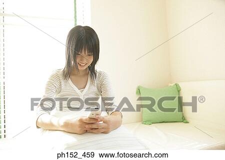 Close-up of a young woman holding a mobile phone and smiling View Large Photo Image Stock Photo - Close-up of a young woman holding a mobile phone and smiling. Fotosearch