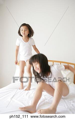 Stock Image - Girl and her sister jumping on the bed. Fotosearch