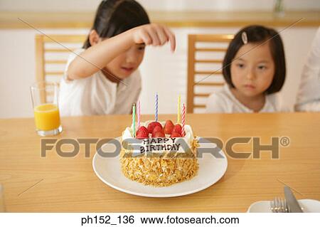 Stock Photograph - Girl and her sister sitting at the table with a birthday cake in front of them. Fotosearch