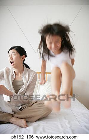 Girl jumping on the bed with her mother sitting behind her View Large Photo Image Stock Photograph - Girl jumping on the bed with her mother sitting behind her. Fotosearch
