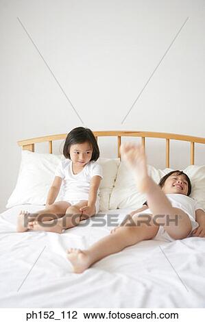 Girl lying on her back with one leg raised and her sister sitting beside her on the bed View Large Photo Image Stock Image - Girl lying on her back with one leg raised and her sister sitting beside her on the bed. Fotosearch