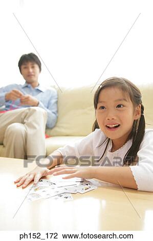 Girl playing a card game with her father sitting in the background View Large Photo Image Stock Image - Girl playing a card game with her father sitting in the background. Fotosearch
