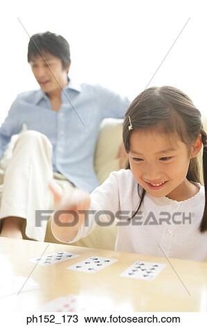 Stock Image - Girl playing a card game with her father sitting in the background. Fotosearch
