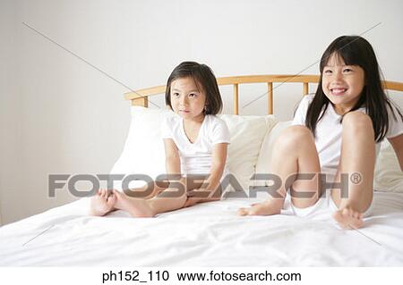 Stock Image - Girl sitting with her sister on the bed. Fotosearch