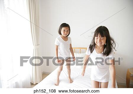 Stock Photo - Girl standing on the bed and looking at her sister. Fotosearch