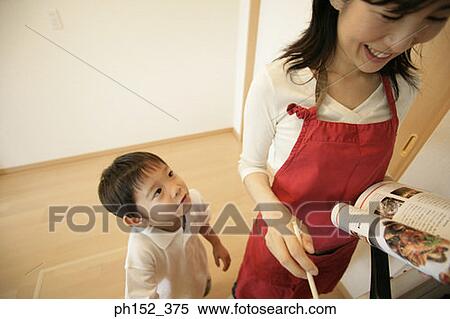 Stock Photography - High angle view of a boy standing beside his mother and cooking with the help of a recipe book. Fotosearch