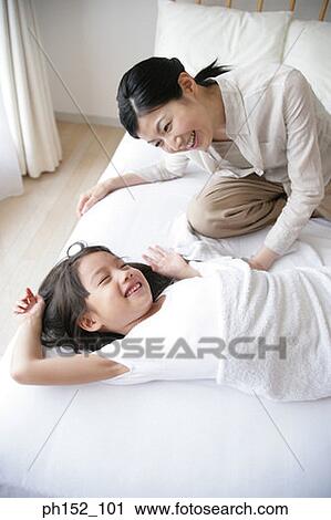 Stock Image - High angle view of a mid adult woman and her daughter laughing on the bed. Fotosearch