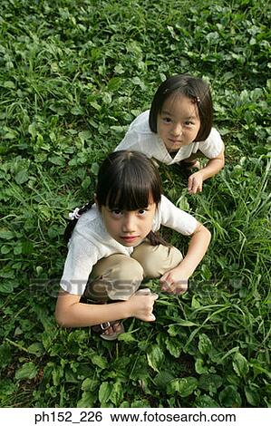Stock Photograph - High angle view of two girls crouching in a park. Fotosearch
