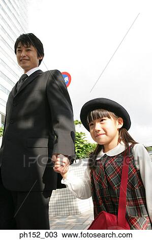 Stock Image - Low angle view of a mid adult man holding his daughter's hand and walking. Fotosearch
