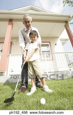Stock Photograph - Low angle view of a senior man teaching his grandson how to play golf. Fotosearch