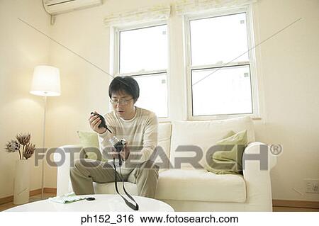 Mature man sitting on a couch and cleaning the lens of a camera View Large Photo Image Stock Photograph - Mature man sitting on a couch and cleaning the lens of a camera. Fotosearch