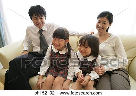 Mid adult couple and their daughters sitting on a couch and smiling View Large Photo Image Stock Image - Mid adult couple and their daughters sitting on a couch and smiling. Fotosearch