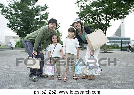Stock Image - Mid adult couple and their two daughters holding shopping bags. Fotosearch