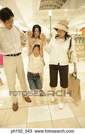 Stock Image - Mid adult couple carrying their son with their daughter behind them in a shopping mall. Fotosearch