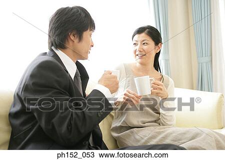Stock Image - Mid adult couple holding cups of coffee and looking at each other. Fotosearch