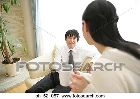 Stock Photo - Mid adult couple holding cups of coffee and looking at each other. Fotosearch