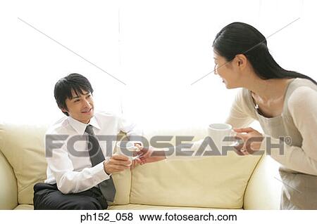 Stock Photo - Mid adult couple holding cups of coffee and looking at each other. Fotosearch