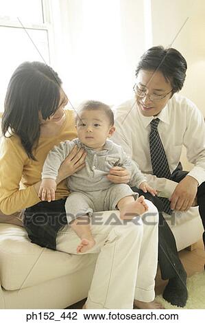 Stock Image - Mid adult couple sitting with their son on a couch. Fotosearch