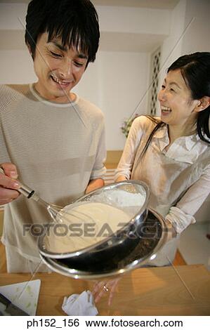 Stock Photograph - Mid adult man preparing batter with a mid adult woman standing beside him. Fotosearch