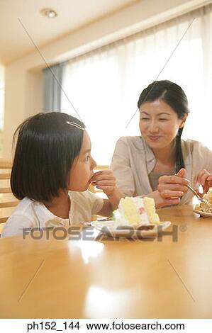 Mid adult woman and her daughter eating a cake View Large Photo Image Picture - Mid adult woman and her daughter eating a cake. Fotosearch