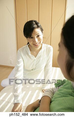 Picture - Mid adult woman and her daughter sitting on the bed and smiling. Fotosearch