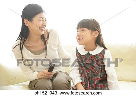 Mid adult woman and her daughter sitting on a couch and smiling View Large Photo Image Stock Image - Mid adult woman and her daughter sitting on a couch and smiling. Fotosearch