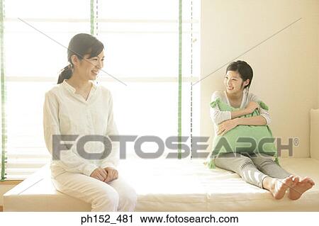 Mid adult woman and her daughter sitting on the bed and smiling View Large Photo Image Stock Image - Mid adult woman and her daughter sitting on the bed and smiling. Fotosearch