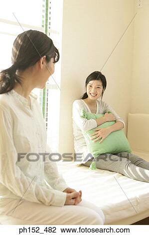 Stock Image - Mid adult woman and her daughter sitting on the bed and smiling. Fotosearch