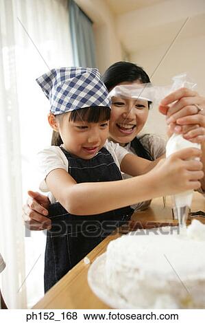 Mid adult woman and her daughter decorating a cake View Large Photo Image Stock Photo - Mid adult woman and her daughter decorating a cake. Fotosearch